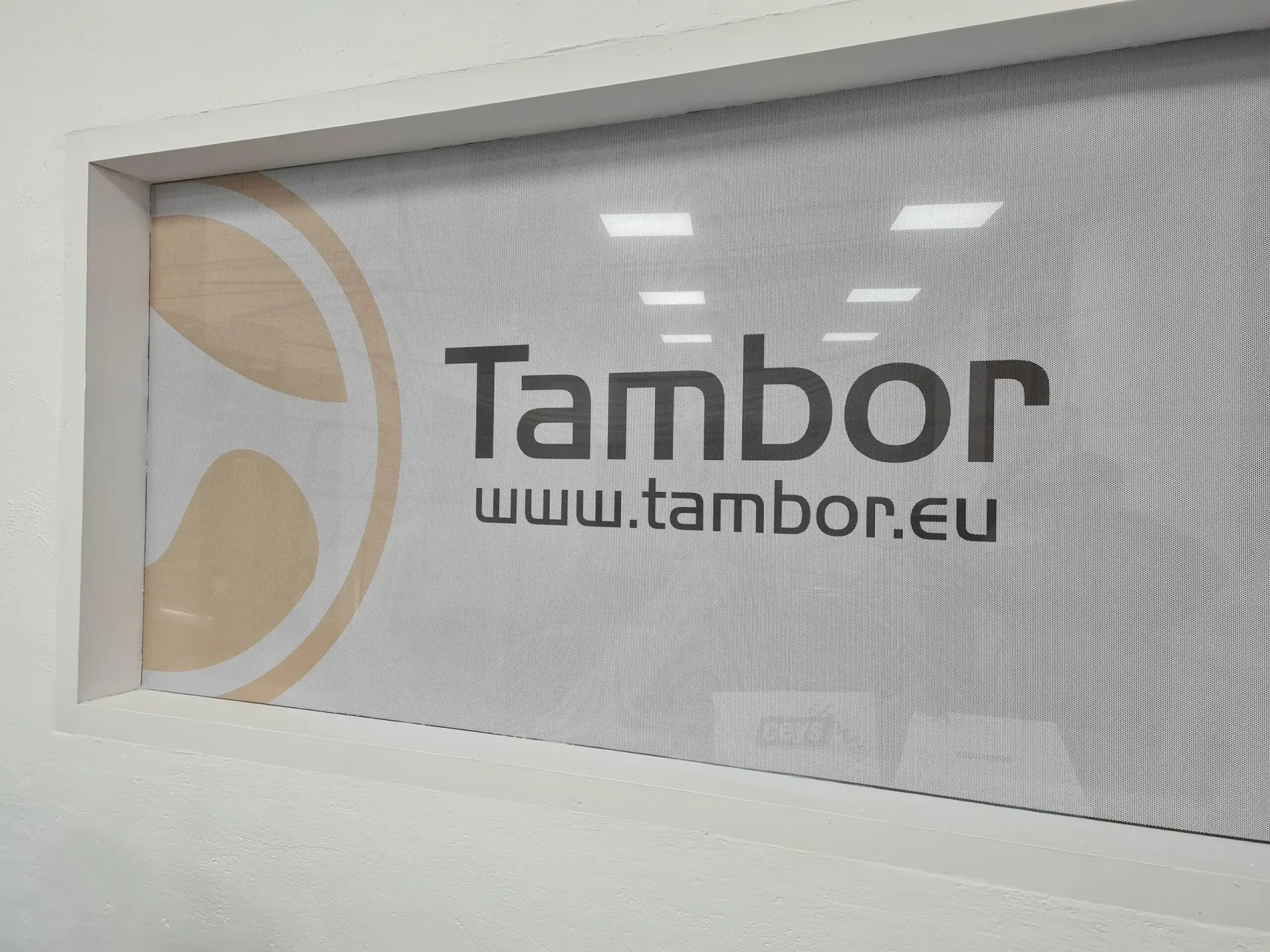 Ventana con el cartel de "Tambor" en texto negro con el logotipo sobre fondo claro; www.tambor.eu se encuentra debajo.
