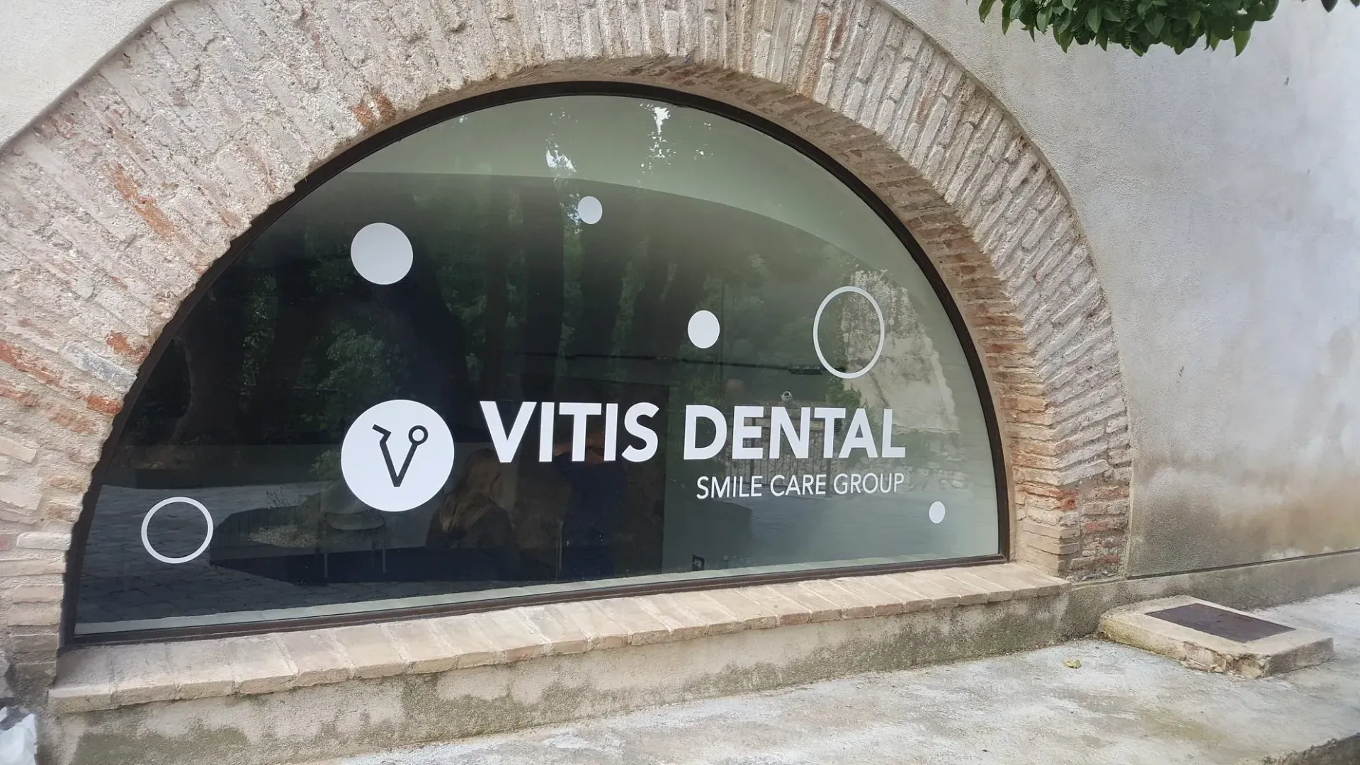 Una clínica dental, Vitis Dental, tras una ventana arqueada. El letrero es blanco sobre vidrio negro. La ventana está enmarcada por ladrillo.