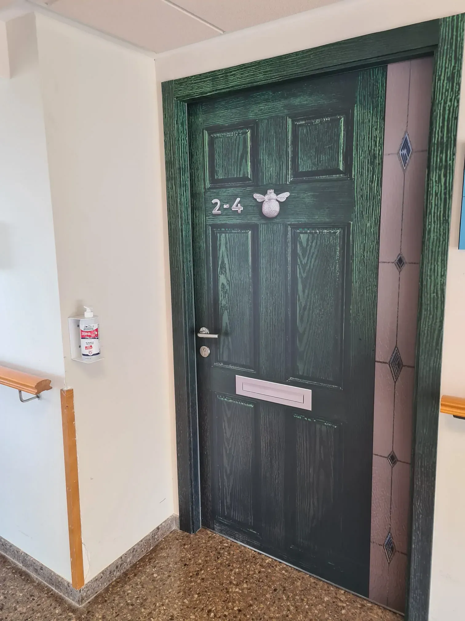 Puerta verde con marco decorativo, con el número "2-4" sobre un tirador. Un pequeño ángel sobre el número de la puerta.