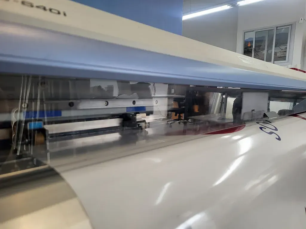 Primer plano de una impresora con un rollo grande de papel blanco. La máquina está en funcionamiento y se está aplicando tinta.