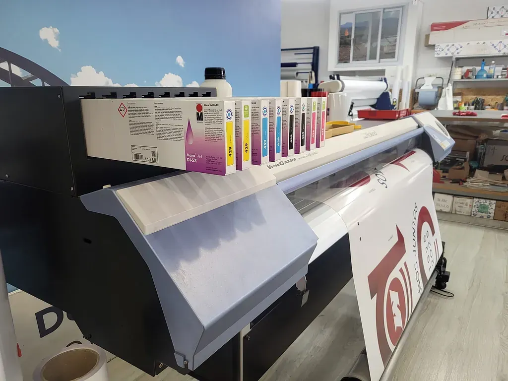 Una impresora de gran formato con cartuchos de tinta de color encima, dentro de una imprenta.