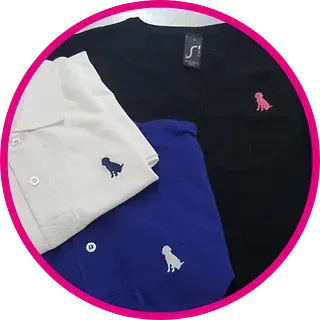 Tres camisetas: blanca, negra y azul, cada una con el logo de un pequeño perro. La camiseta negra tiene el logo rosa, mientras que las demás son azules.