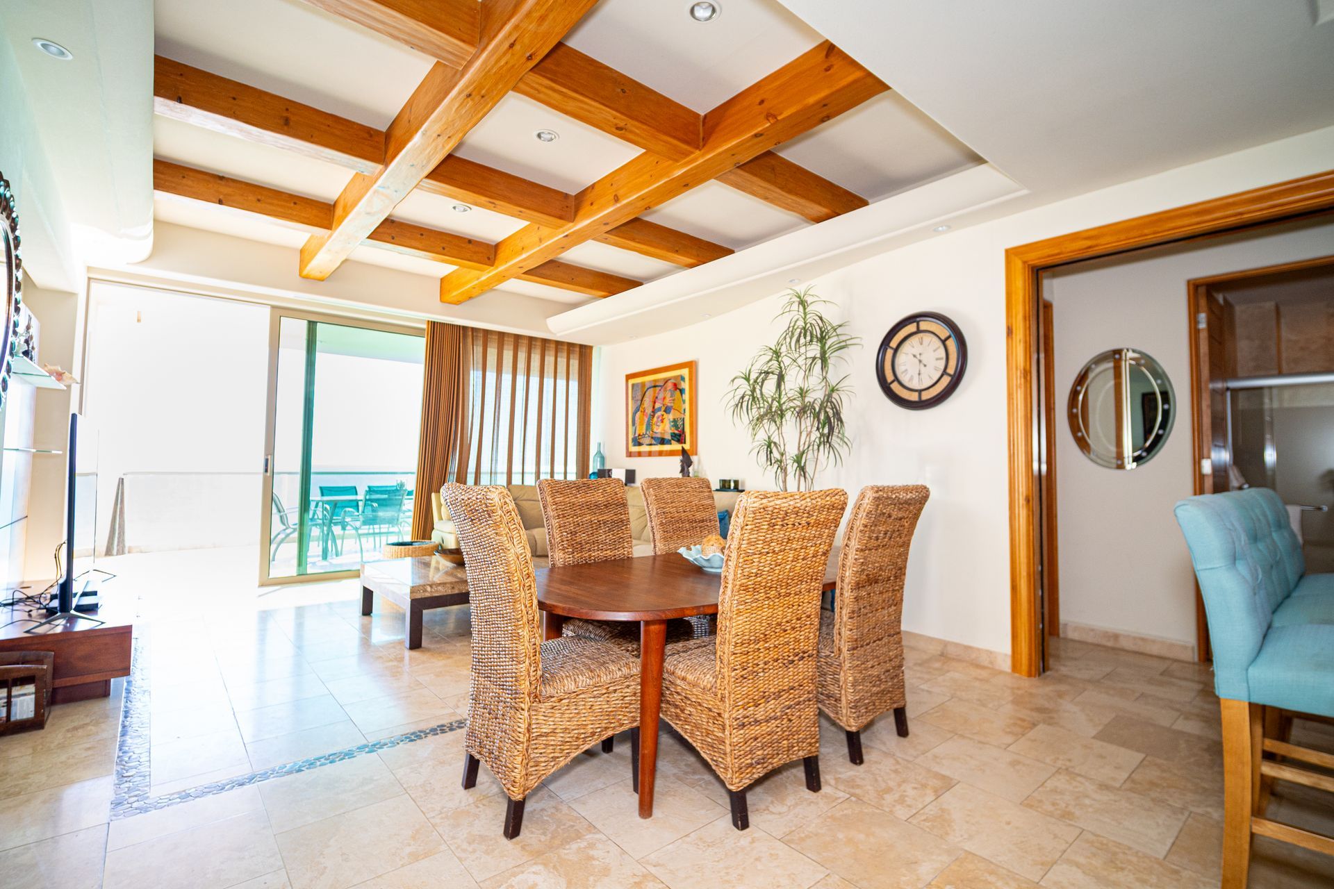 Bright dining room with wicker chairs, wooden table, exposed beam ceiling, and ocean view through sliding doors