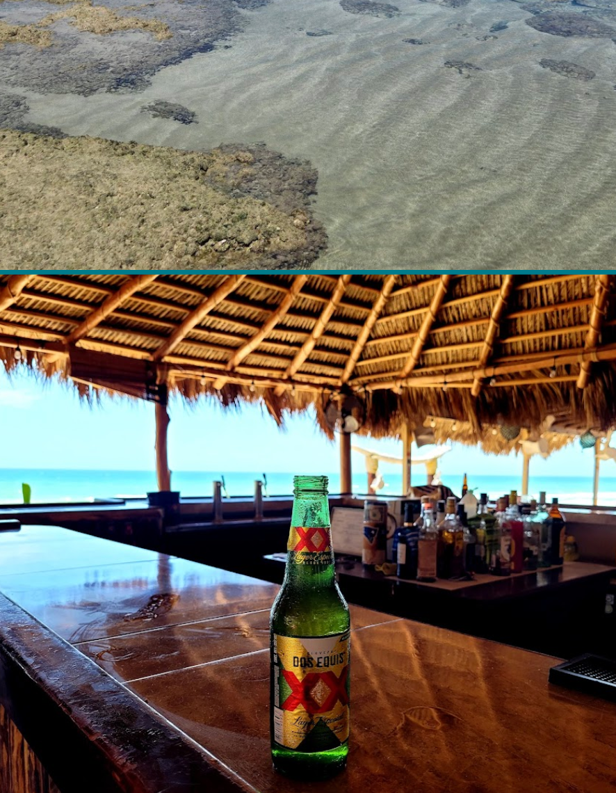 Shallow seawater and a beach bar with a beer bottle on a wooden table overlooking the ocean