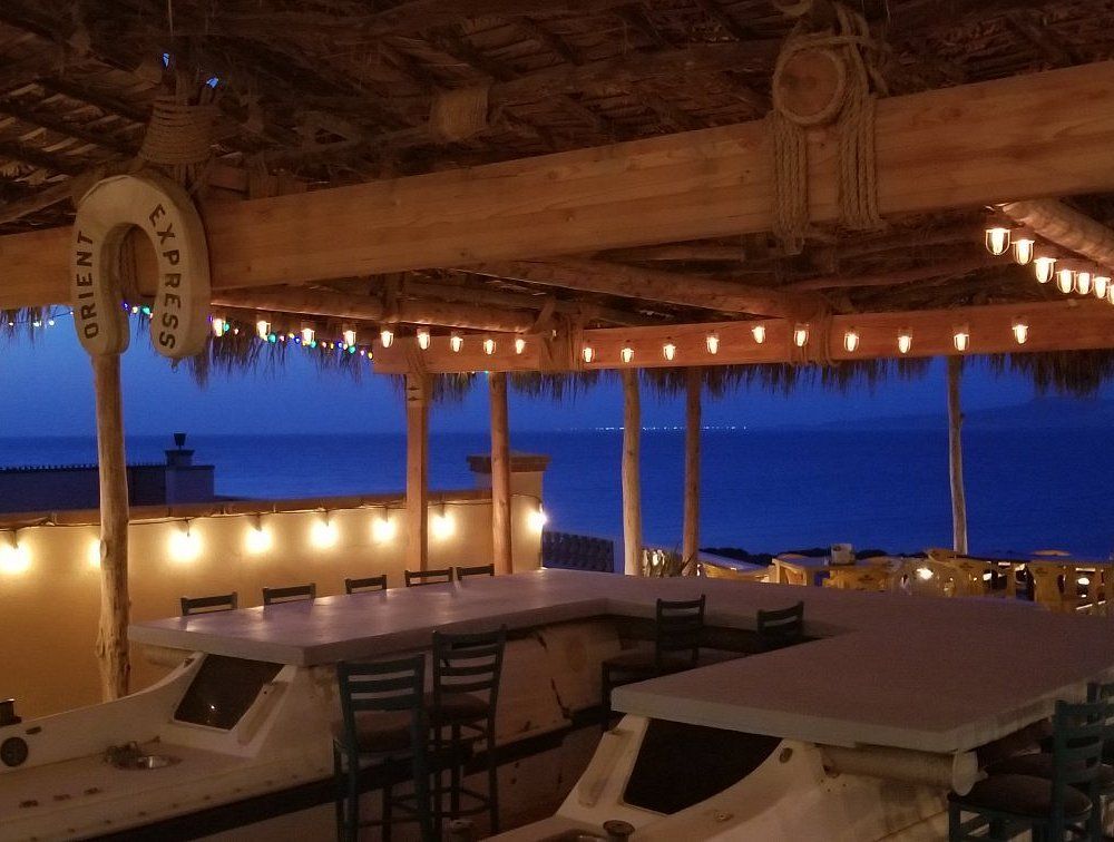 Tropical beachfront patio at dusk with string lights, tables, and ocean view