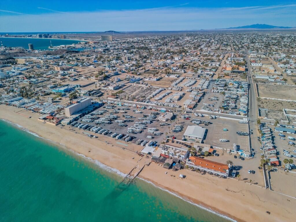 Aerial view of a sandy beach, turquoise water, and a dense coastal city with docks and streets