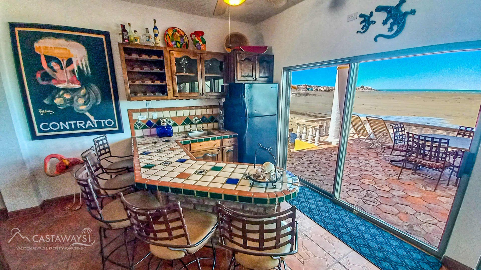 Balcony with glass table and chairs overlooking a sunny beach and ocean from a high-rise condo