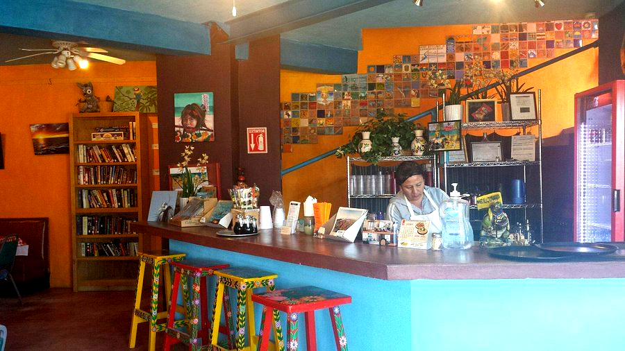 Colorful café interior with a long bar, stools, hanging lights, and a person behind the counter