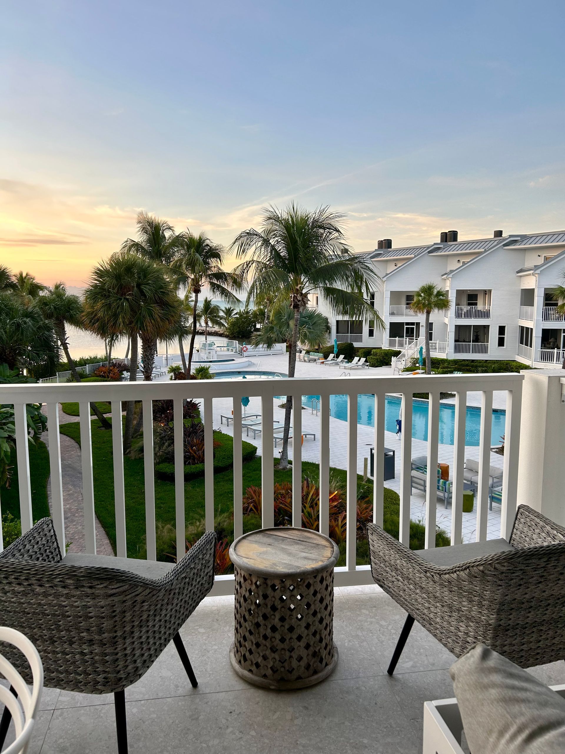 Balcony with seating area overlooking pool and palm trees at Maison 203.