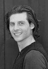 Un jeune homme aux cheveux longs sourit sur une photo en noir et blanc.