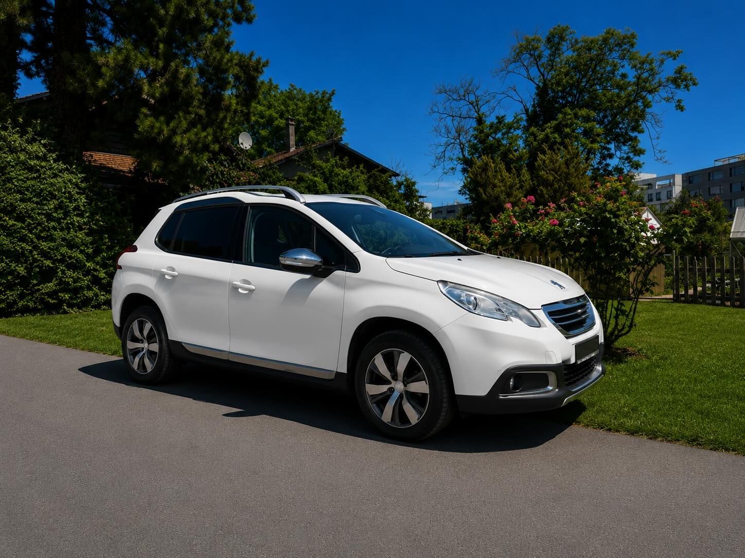 Un SUV blanc est garé dans une allée, bordée de haies vertes, sous un ciel bleu azur.