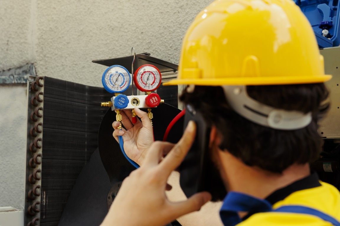 Un trabajador con casco amarillo inspecciona los manómetros del sistema de climatización en una unidad exterior.