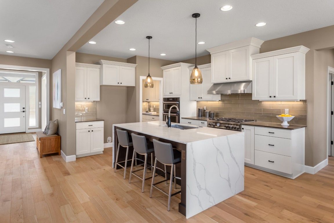 Cocina moderna y luminosa con gabinetes blancos, isla de mármol, lámparas colgantes y pisos de madera noble.