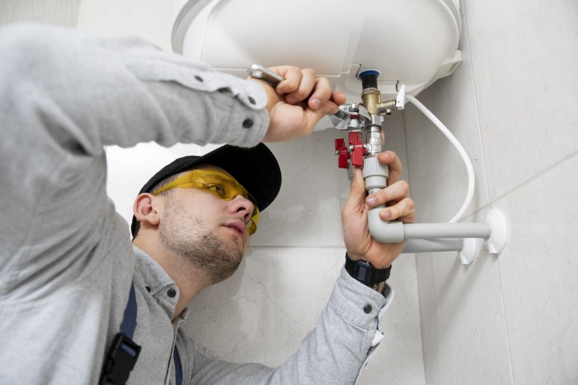 Un fontanero repara una tubería de lavabo debajo de un accesorio de baño blanco, utilizando una llave inglesa.