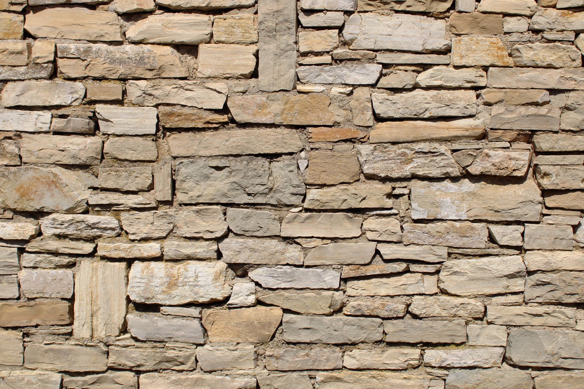 Mur en pierre, briques de tailles et de nuances variées, beiges et grises.