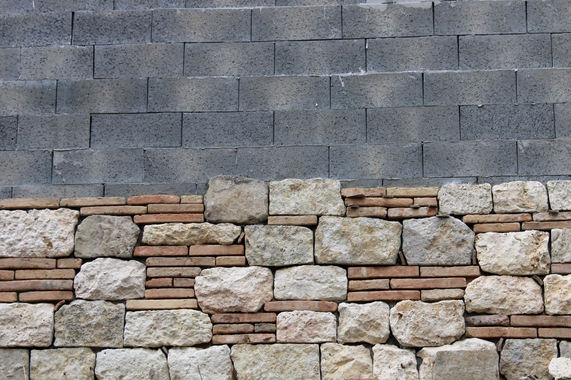 Section de mur en pierre bicolore. Partie supérieure : blocs gris foncé ; partie inférieure : pierre claire avec accents de briques rouges.