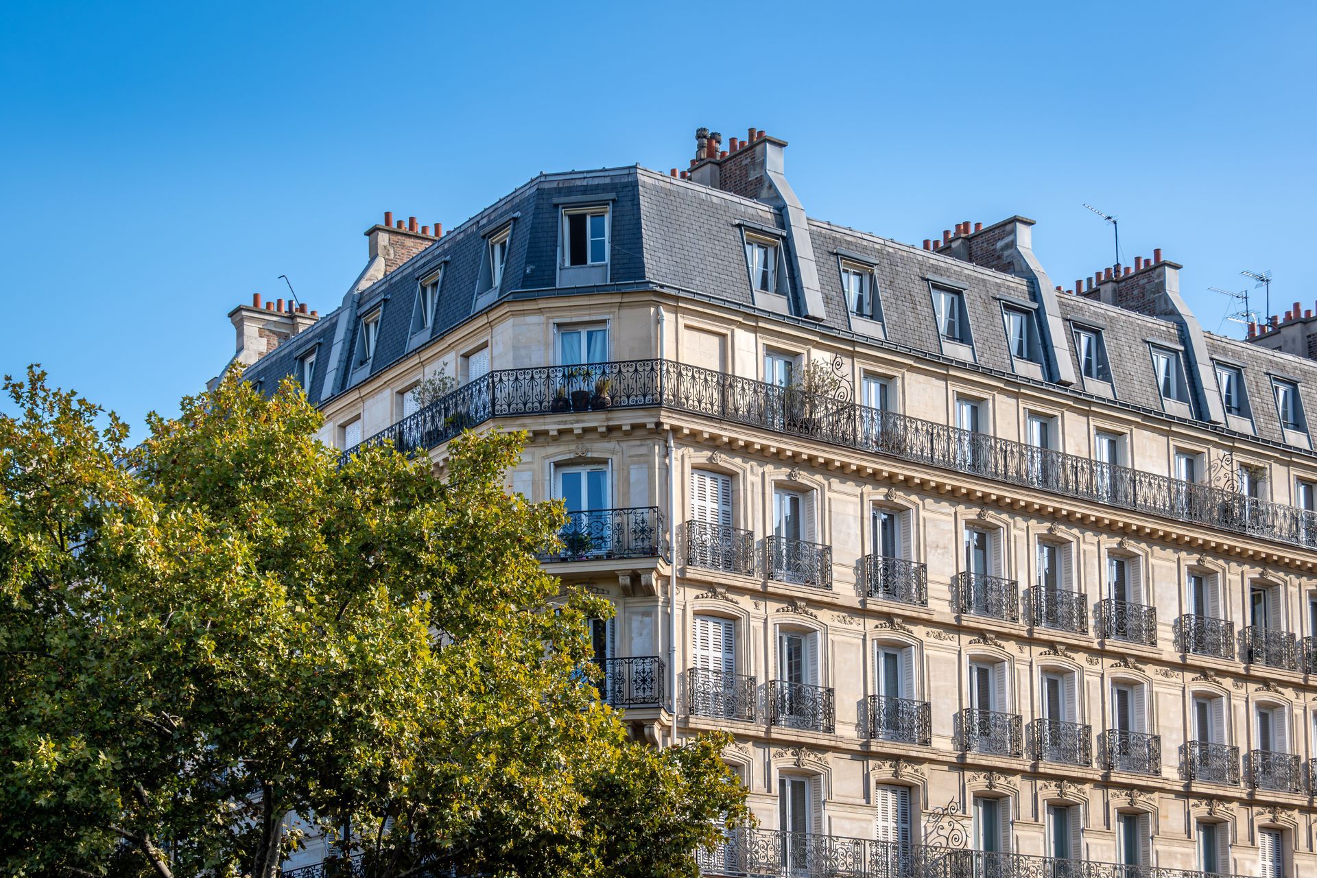 Immeuble parisien avec toit mansardé, balcons et lucarnes, se détachant sur un ciel bleu.