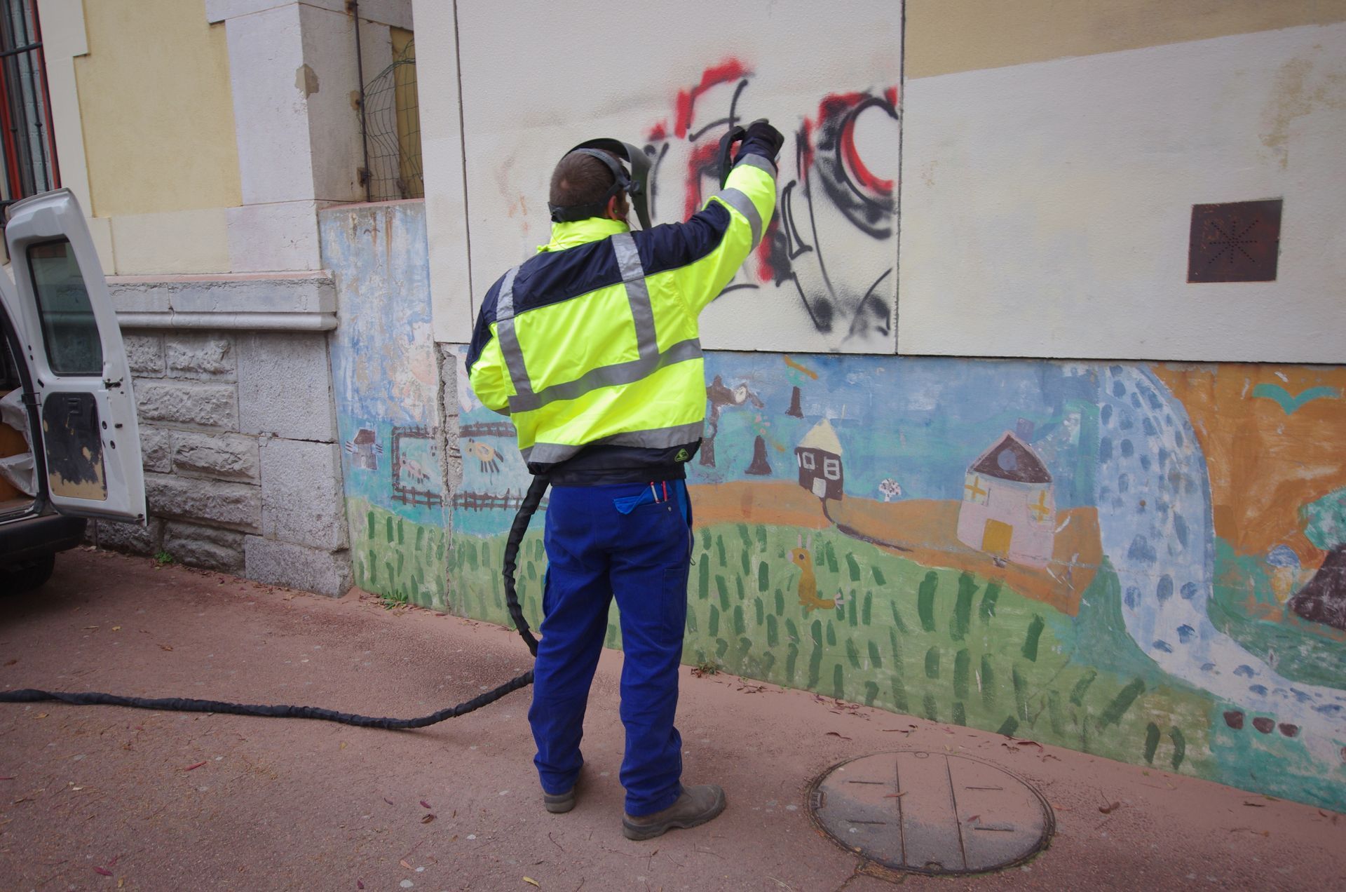 Personne portant des vêtements réfléchissants enlevant des graffitis d'un mur à l'aide d'une sableuse.