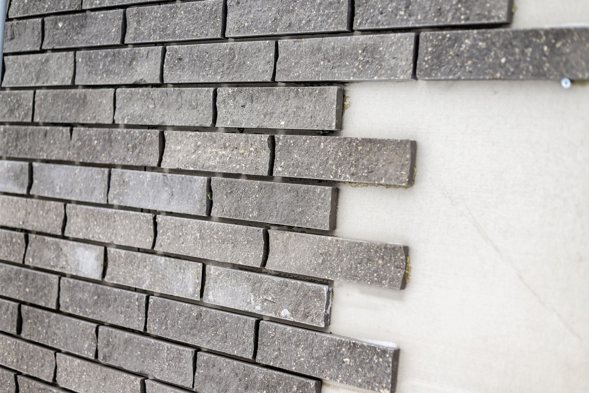 Pose d'un parement en briques grises sur un mur blanc, gros plan sur la construction.