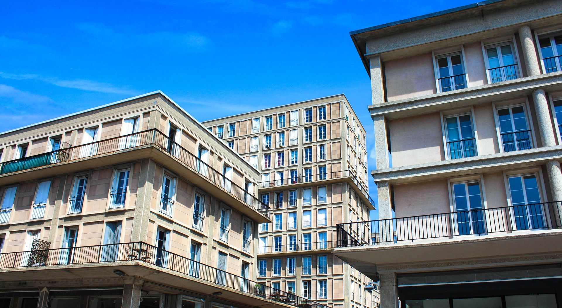 Vue en contre-plongée de plusieurs immeubles d'appartements beiges se détachant sur un ciel bleu vif.