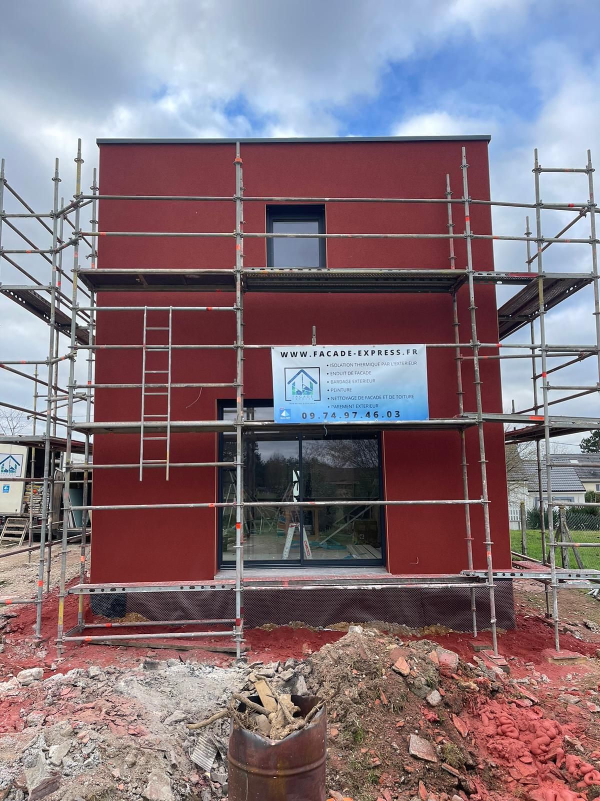 Bâtiment rouge en construction avec échafaudages, fenêtres et une enseigne.