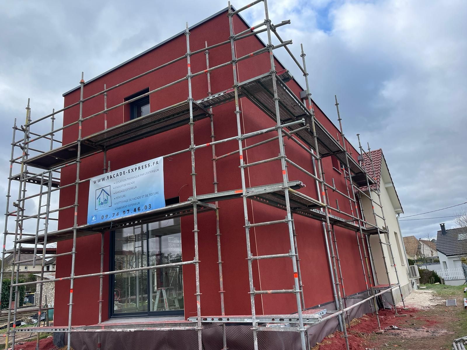 Maison rouge en construction, des échafaudages entourent le bâtiment.