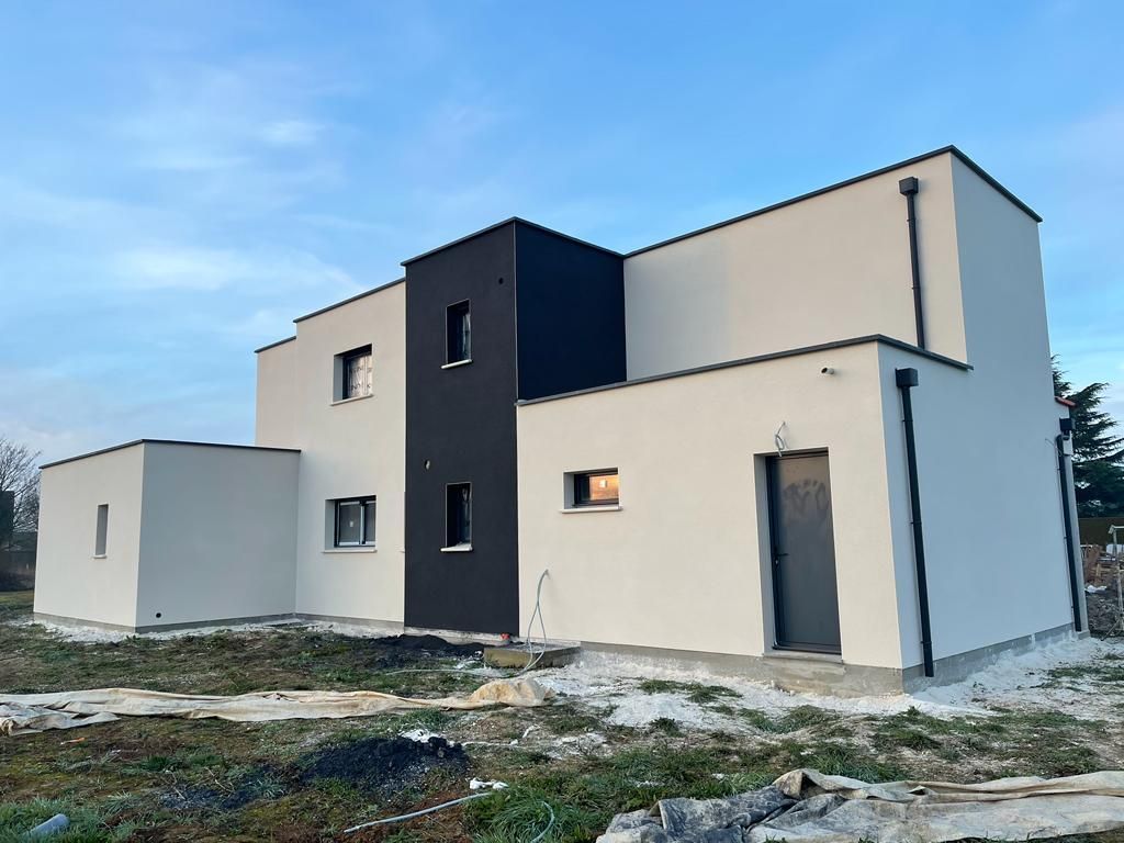 Maison moderne à deux étages, extérieur beige clair, partie accentuée de noir, porte grise, sur fond de ciel nuageux.