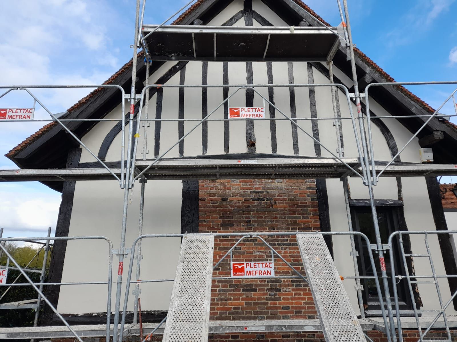 Échafaudages autour d'une maison à colombages en cours de rénovation. Façade en briques et en stuc blanc.