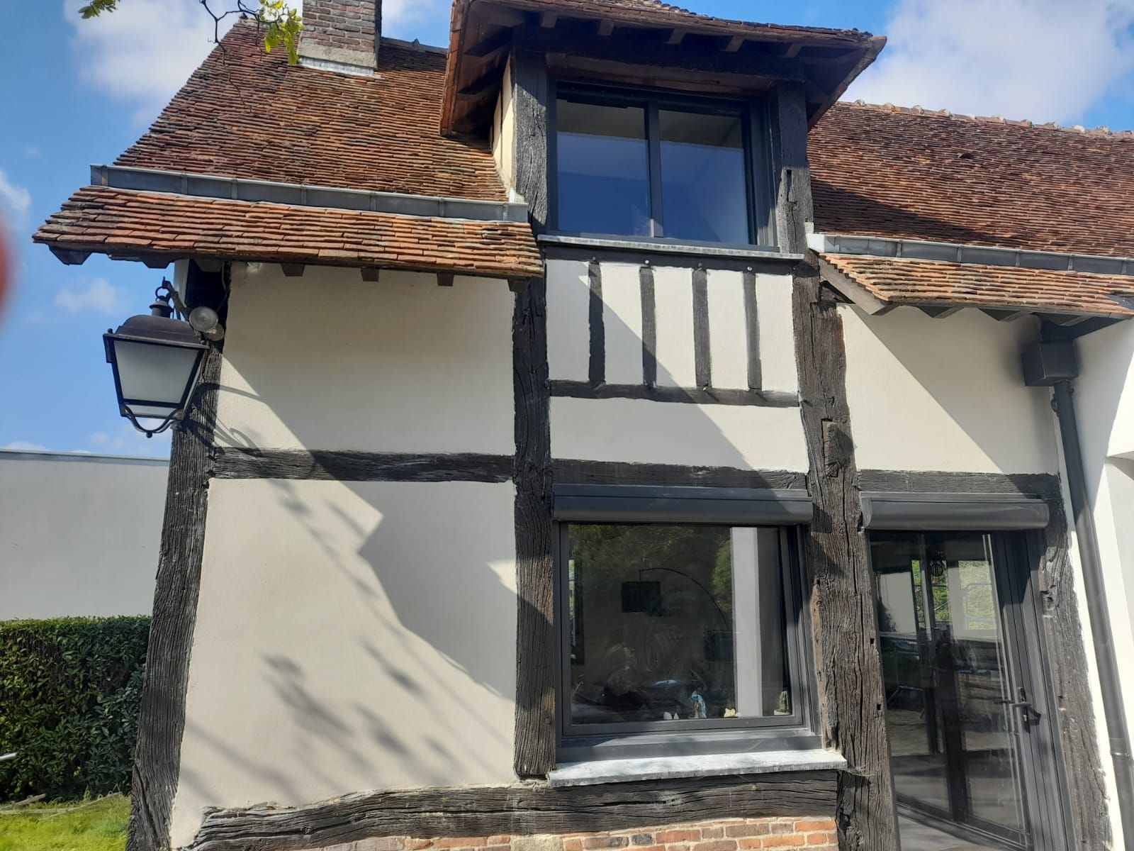 Bâtiment de style Tudor avec toit de tuiles rouges, colombages et murs clairs. Un lampadaire est fixé sur le côté.
