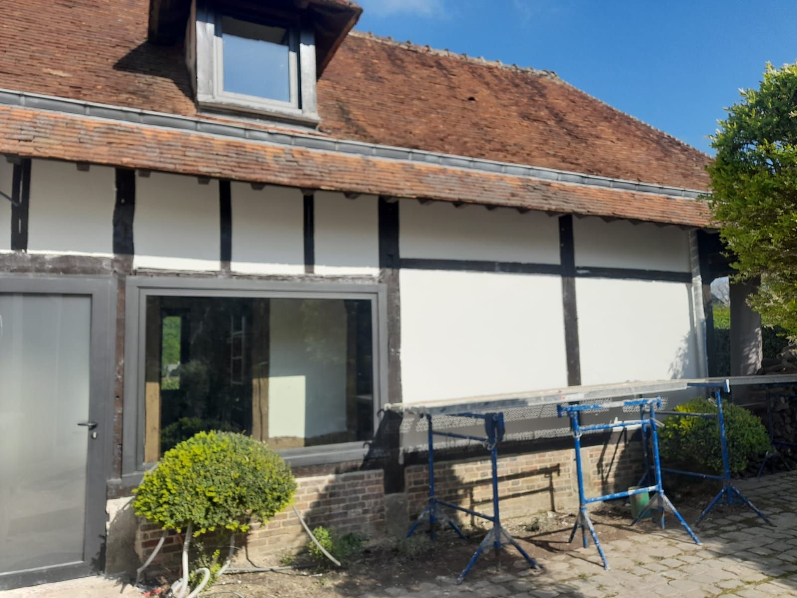 Extérieur d'une maison à colombages avec murs blancs, poutres sombres et toit de tuiles rouges, échafaudages.