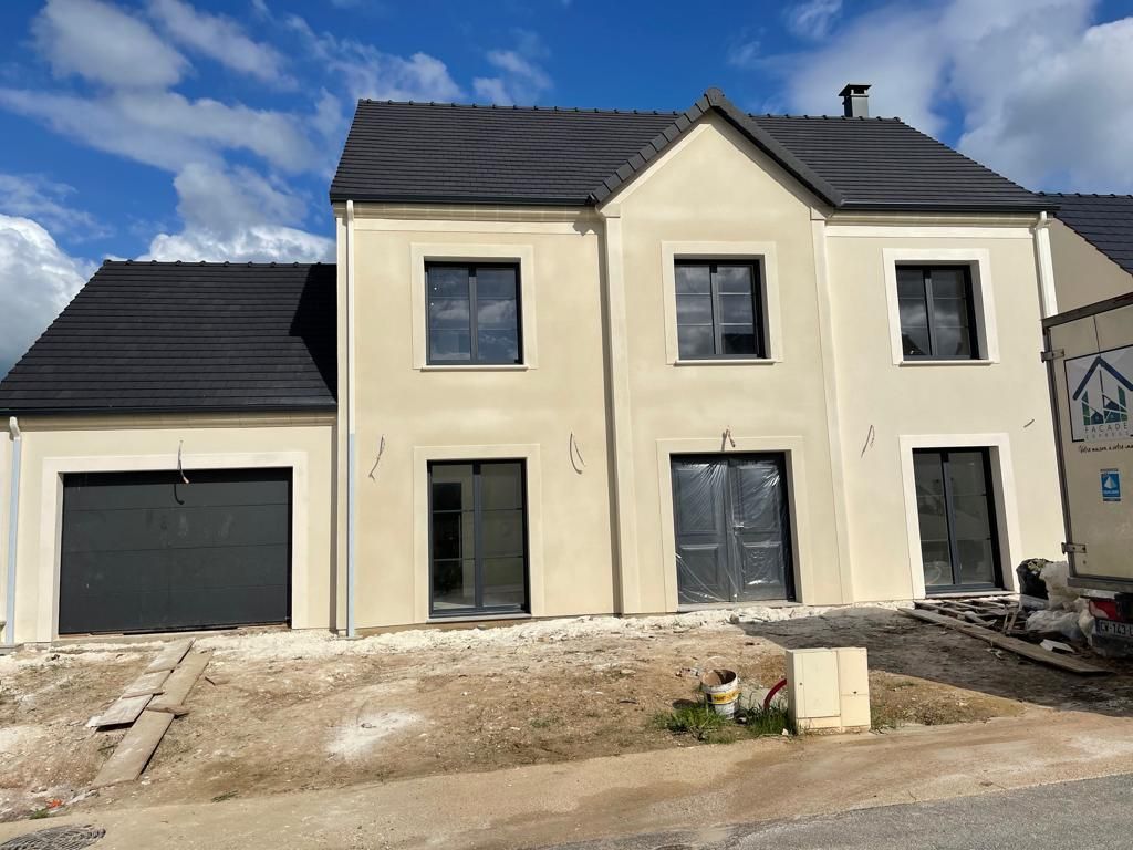 Maison à deux étages avec toit noir et garage. Façade beige, fenêtres et porte de garage gris foncé. Chantier.