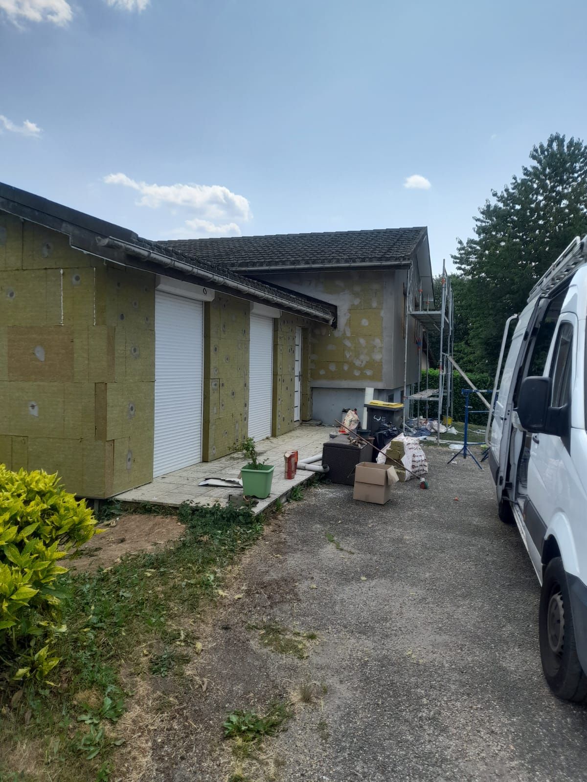 Façade d'un bâtiment en construction avec isolation apparente, volets roulants et une camionnette stationnée.