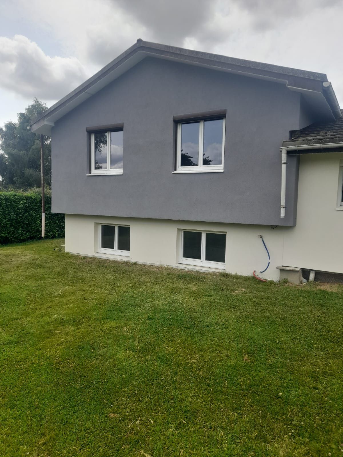 Maison grise à deux étages avec des fenêtres à encadrement blanc, située sur une pelouse verte.