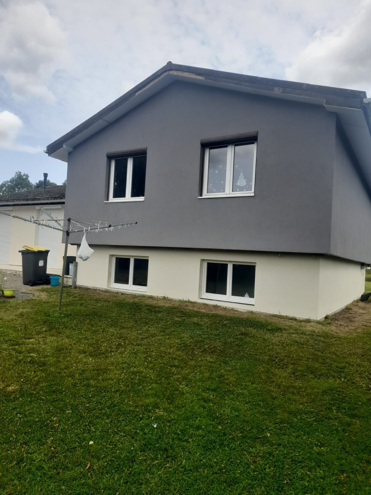 Maison grise et beige aux fenêtres à cadre blanc, située sur une pelouse verte.