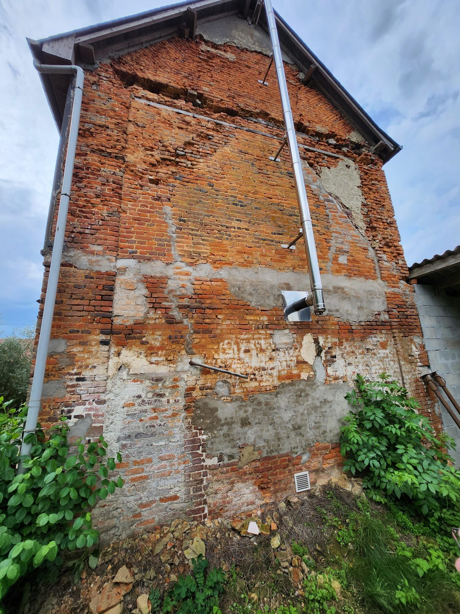 Bâtiment en briques présentant d'importants dommages structurels : fissures, briques manquantes et mortier qui s'effrite.