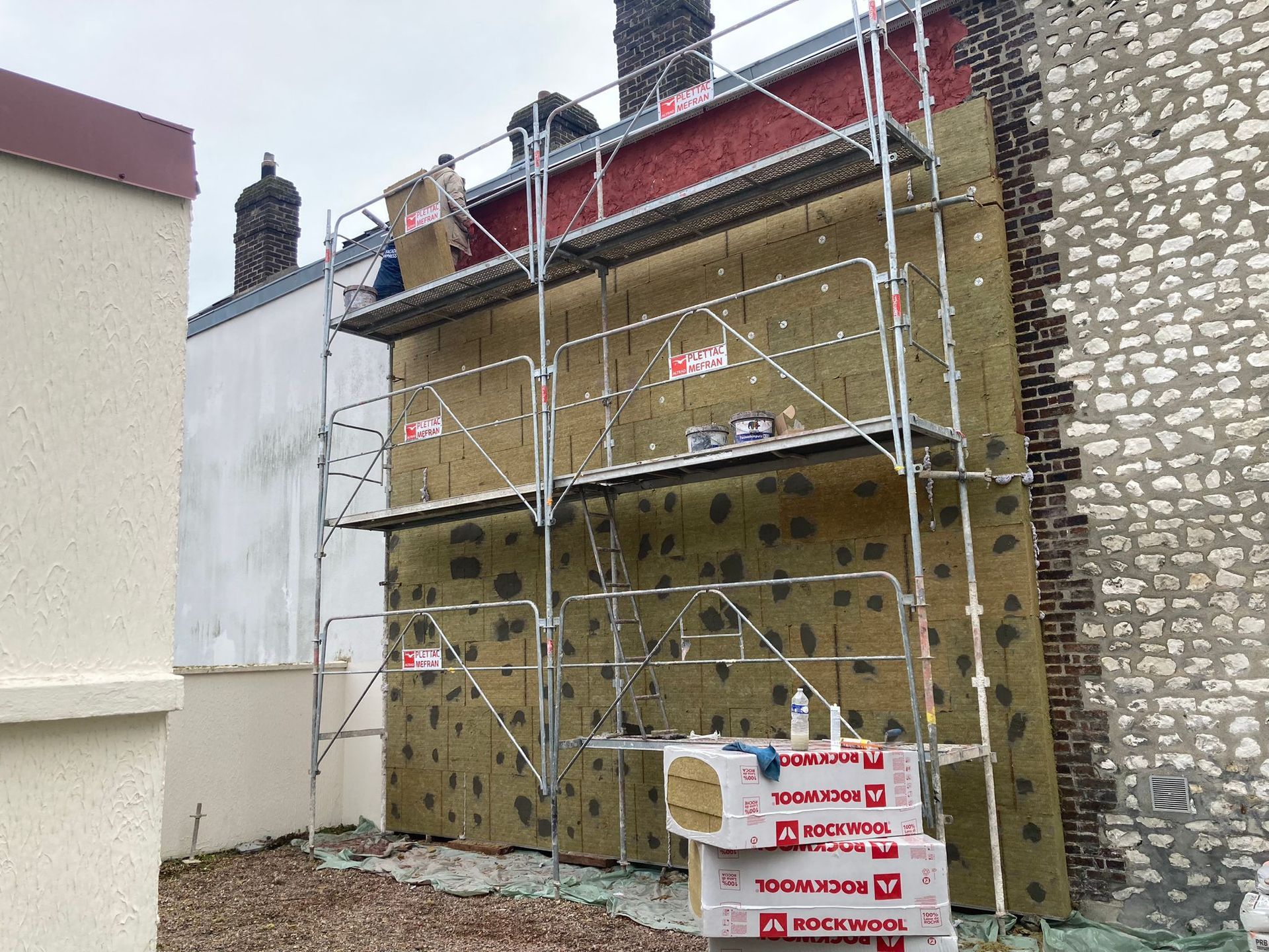 Projet d'isolation des murs extérieurs : échafaudage, panneaux isolants, bâtiment, ciel, matériaux de construction.