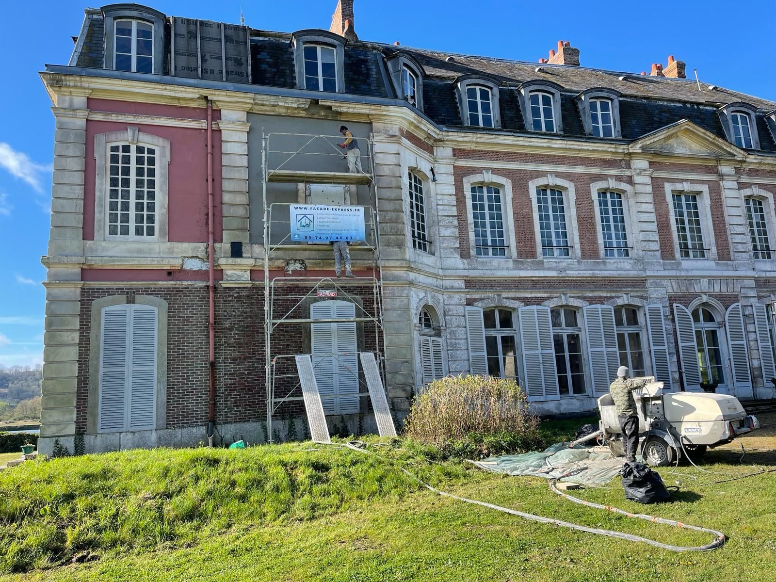 Grand bâtiment orné en rénovation. Échafaudages, façade partiellement visible, pelouse, ciel dégagé.