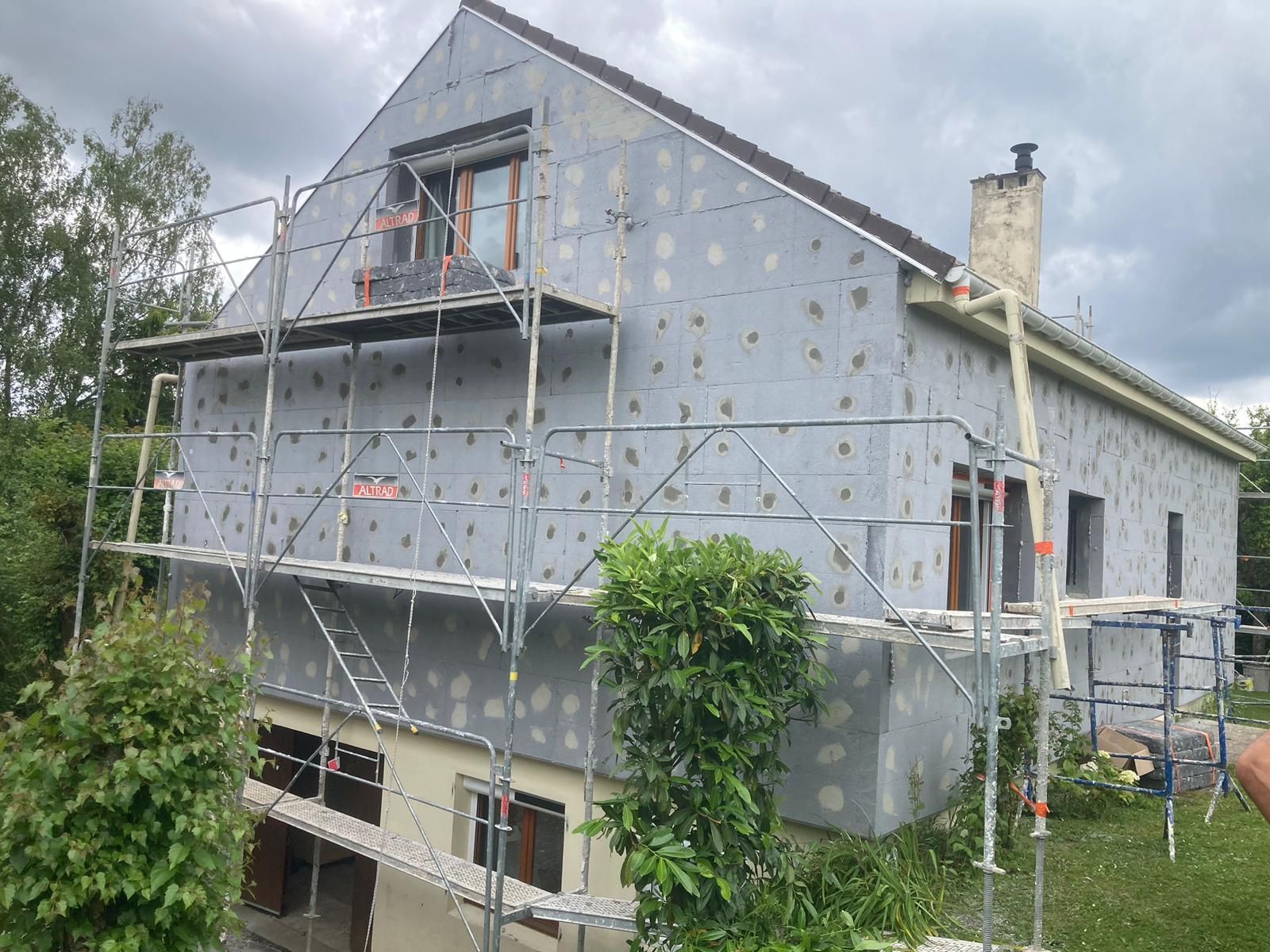 Maison en construction, recouverte d'isolant gris et surmontée d'échafaudages.