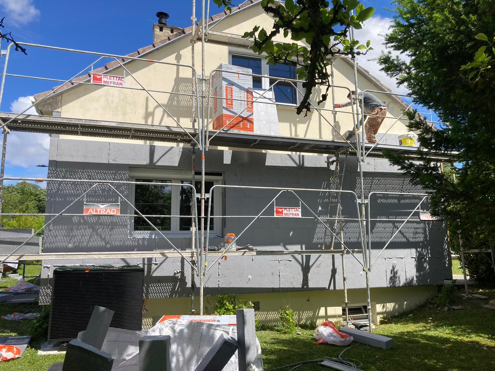 Façade d'une maison en rénovation avec échafaudages. Pose de panneaux isolants gris, ouvrier sur l'échafaudage.