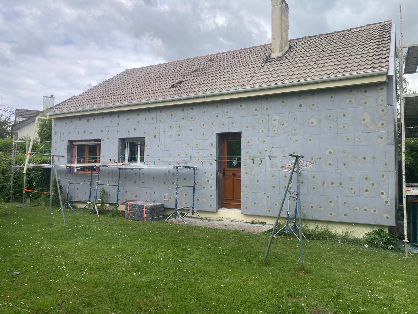 Extérieur de la maison avec panneaux d'isolation installés, échafaudage, porte, fenêtres et cheminée.