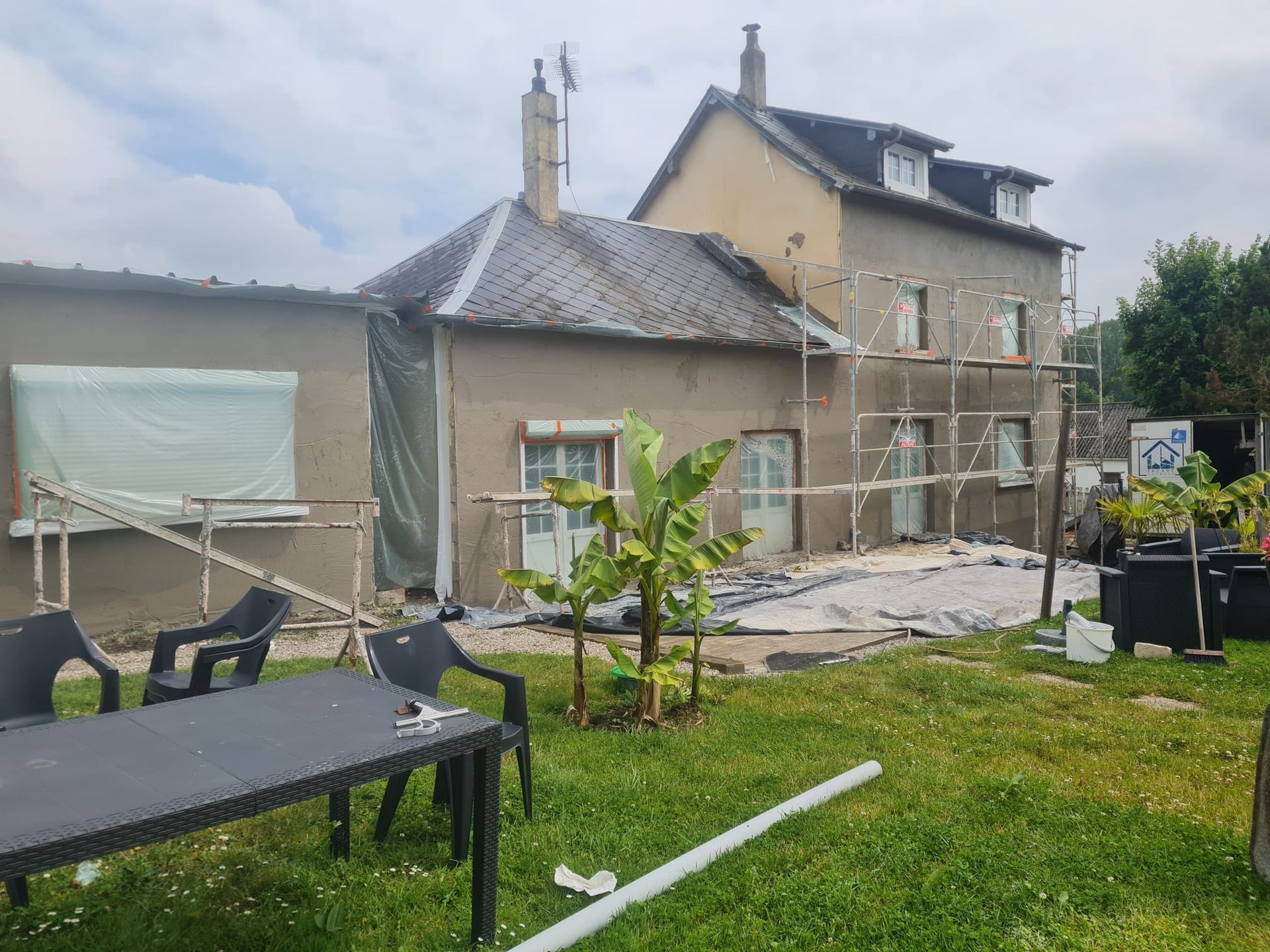 Vue arrière d'une maison à deux étages en rénovation, avec échafaudages, murs apparents et débris.