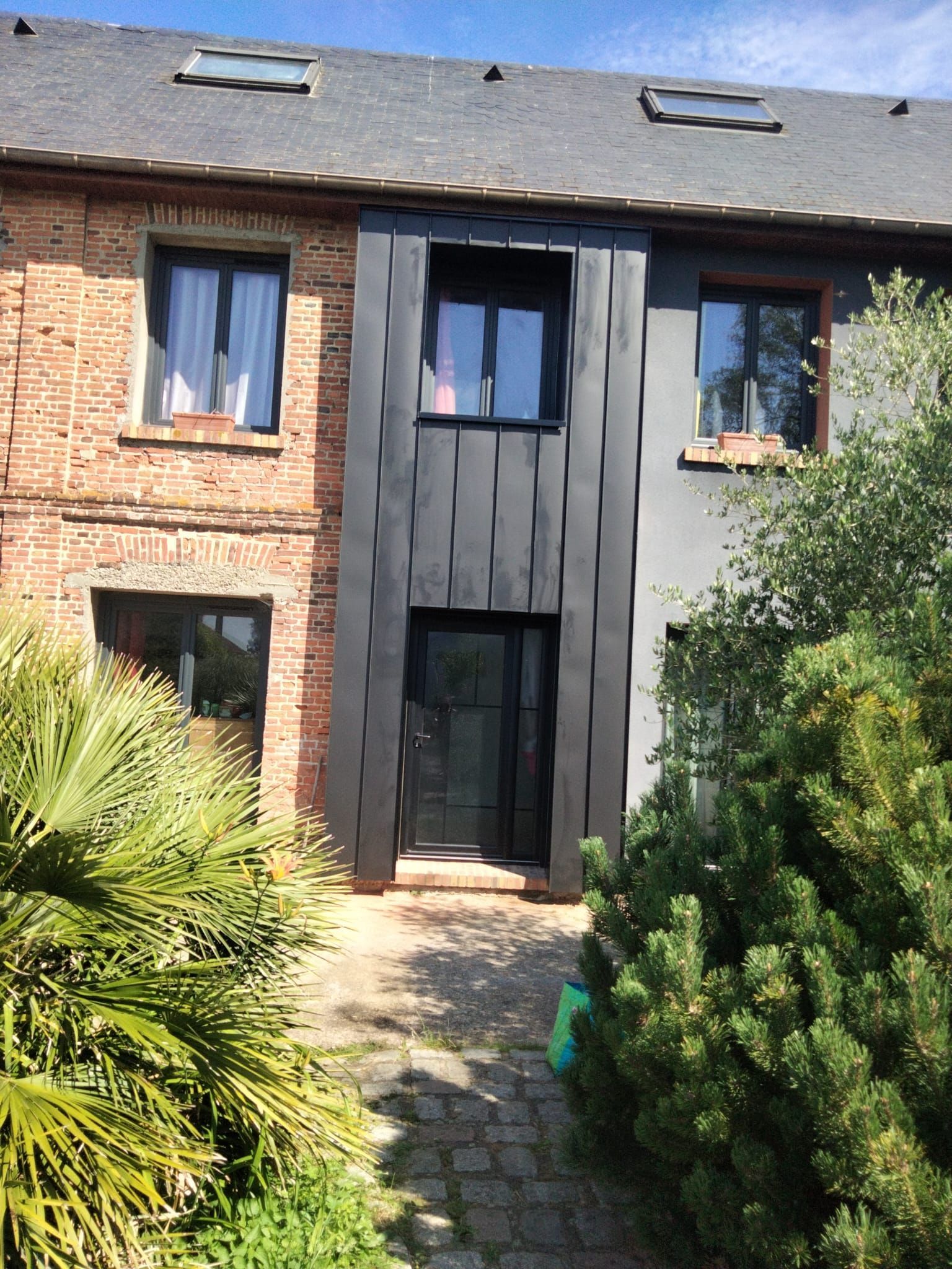 Un bâtiment de deux étages avec une façade noire et des murs, une porte, des fenêtres et de la verdure en briques grises.