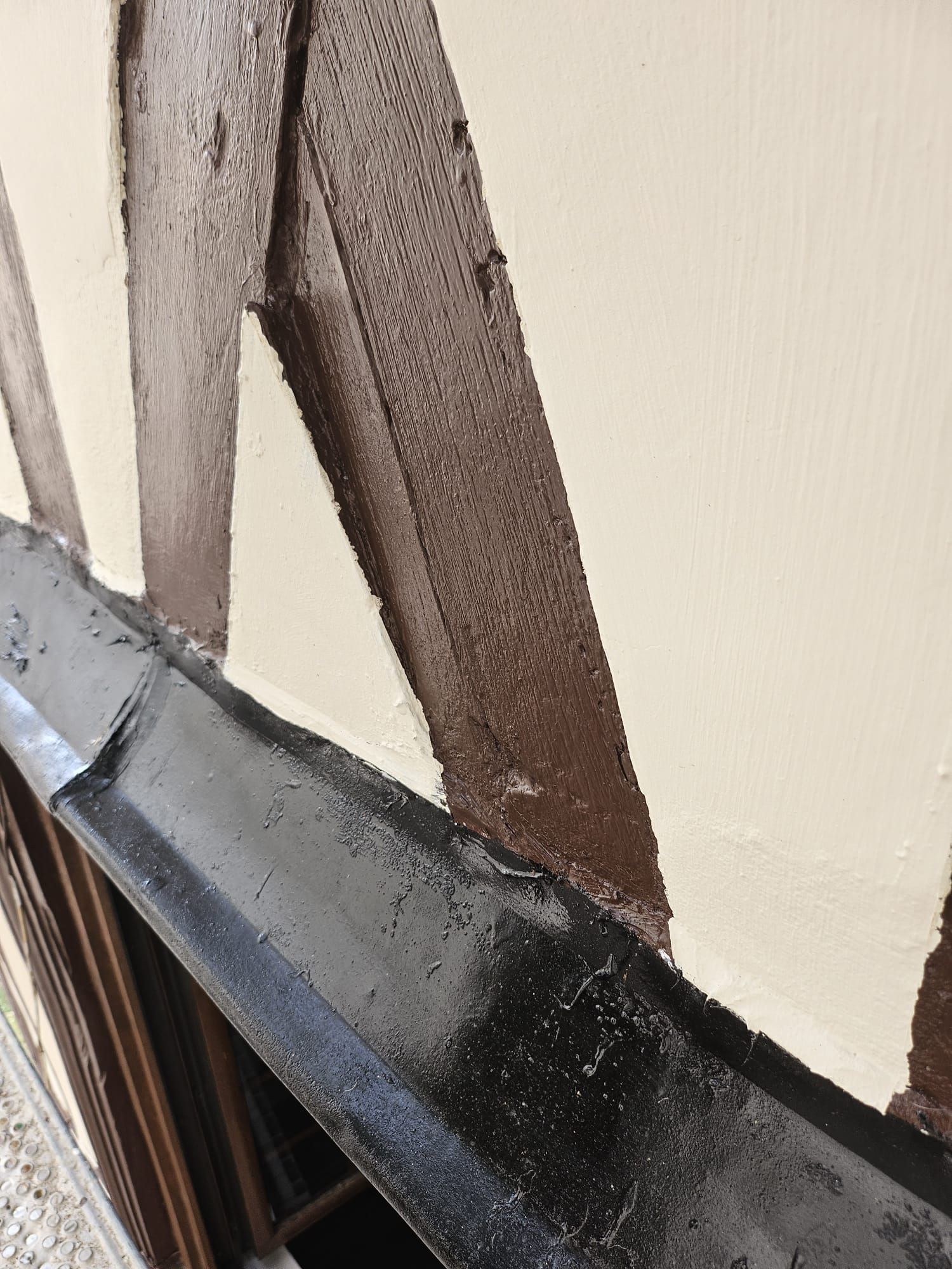 Charpente en bois brun sur un mur crème, avec une gouttière noire.