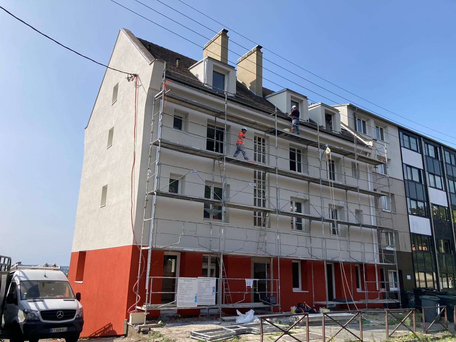 Façade du bâtiment en rénovation ; échafaudages, ouvriers, peinture rouge et blanche.