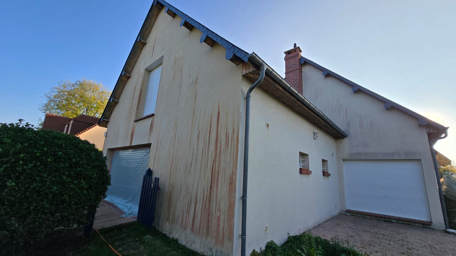 Maison à deux étages à la façade patinée par le temps. La lumière du soleil inonde la structure. La porte du garage est fermée.