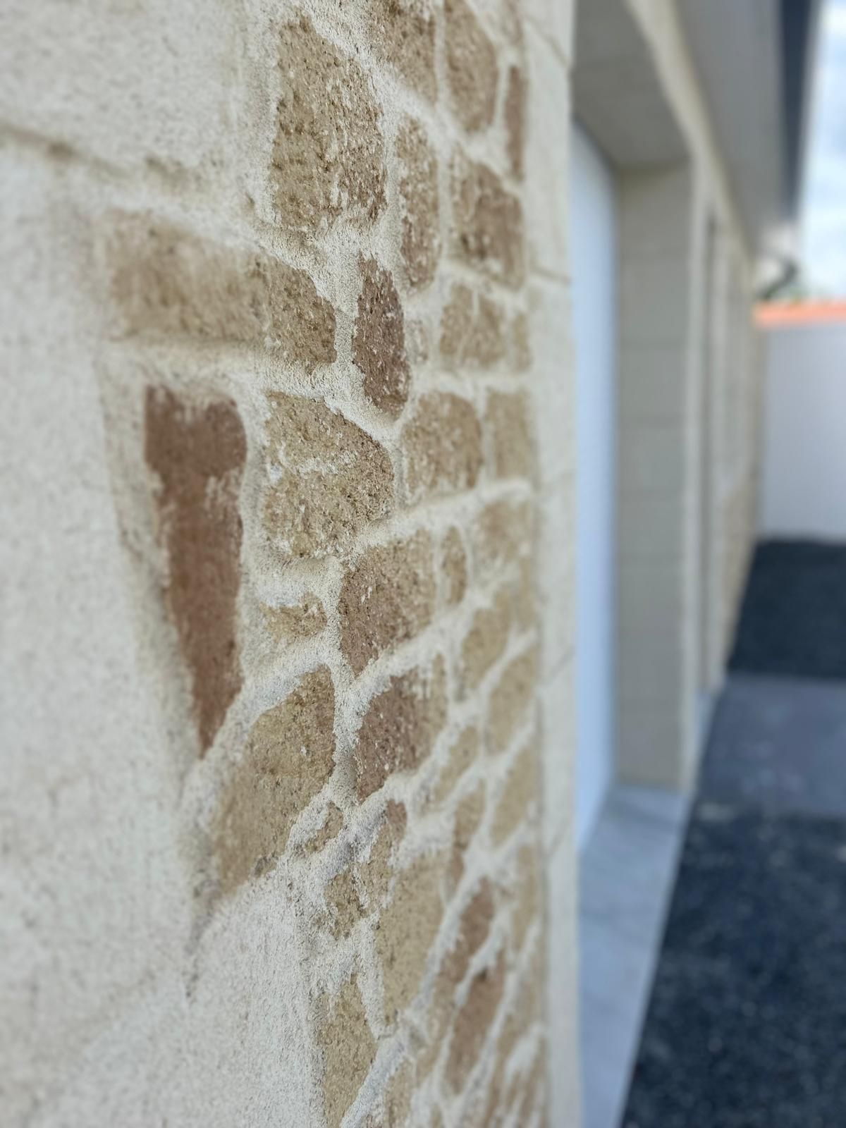 Gros plan sur un mur en pierre beige clair avec des pierres brun foncé et un mortier blanc.