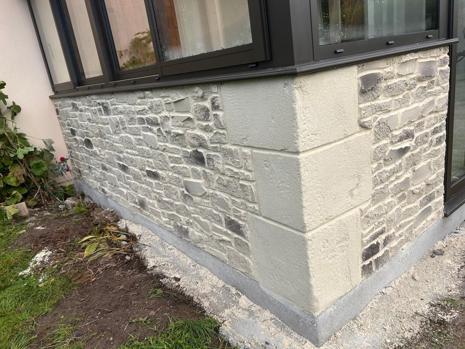 Angle extérieur d'une maison en pierre avec de grandes fenêtres, une maçonnerie détaillée et un mortier clair.