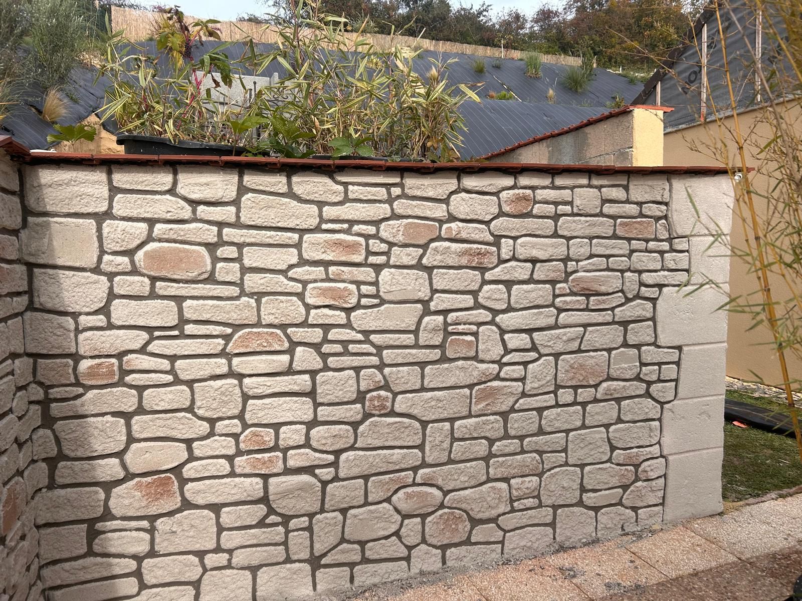 Mur en pierre avec un mortier foncé, surmonté d'une bordure brune.