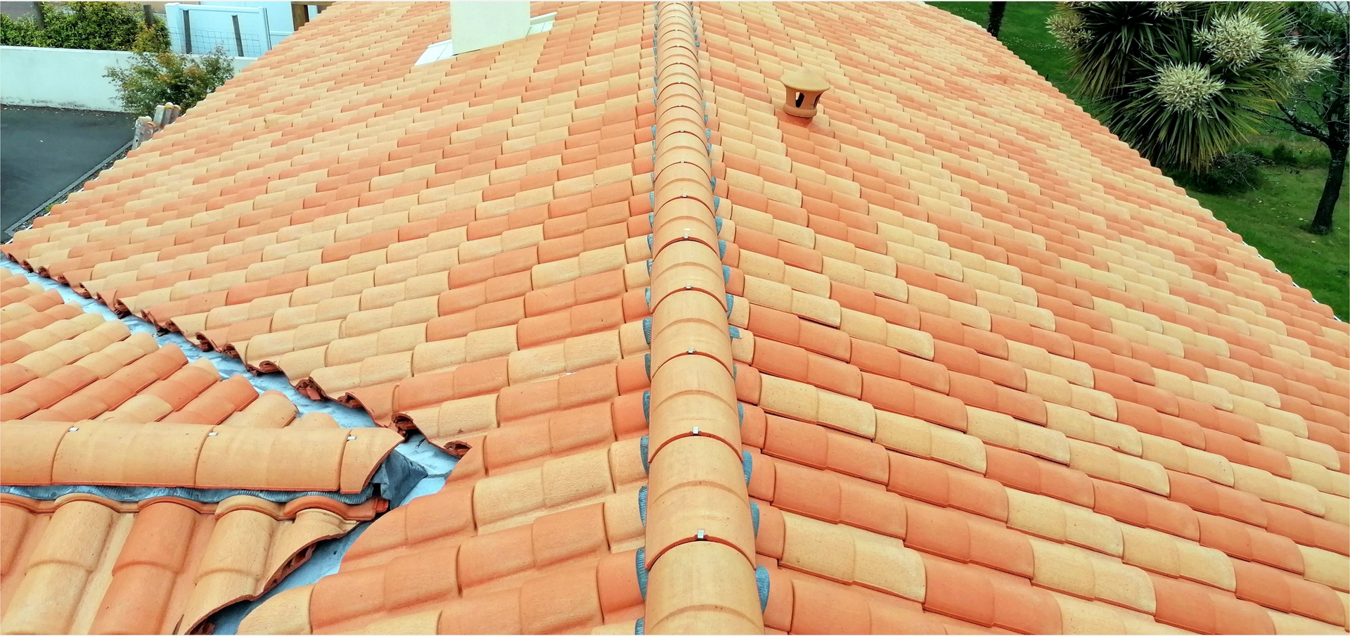 Vue aérienne d'un toit de tuiles en terre cuite, avec une arête centrale et une cheminée visibles.