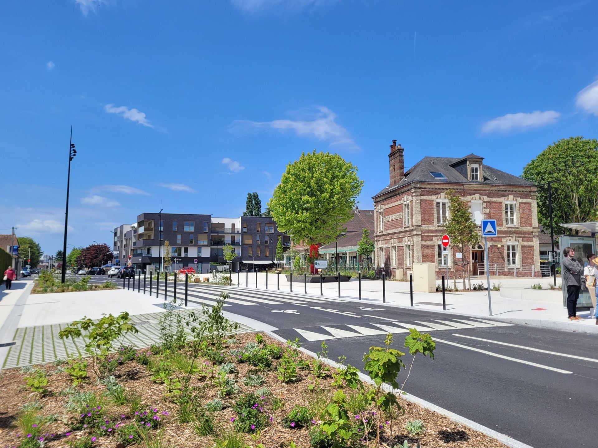 Bois-Guillaume - Place de la ville avec de nouveaux bâtiments et un bâtiment en briques, journée ensoleillée.